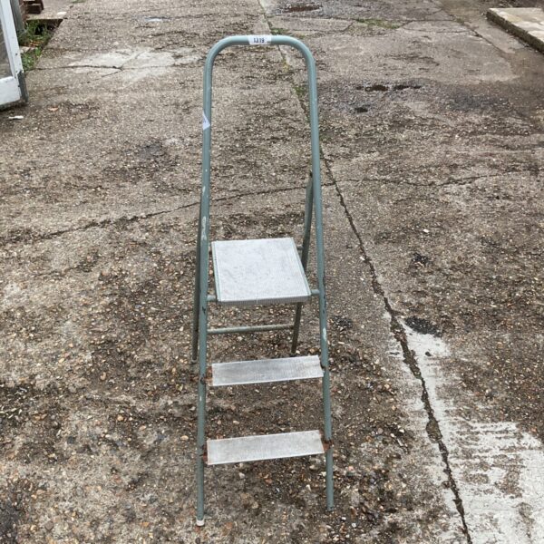 Vintage three-step metal folding ladder in a garden setting.