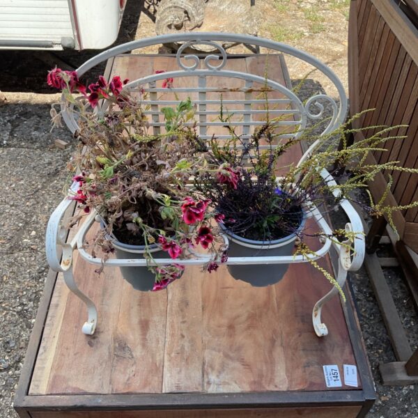 White metal miniature garden bench displaying potted plants.