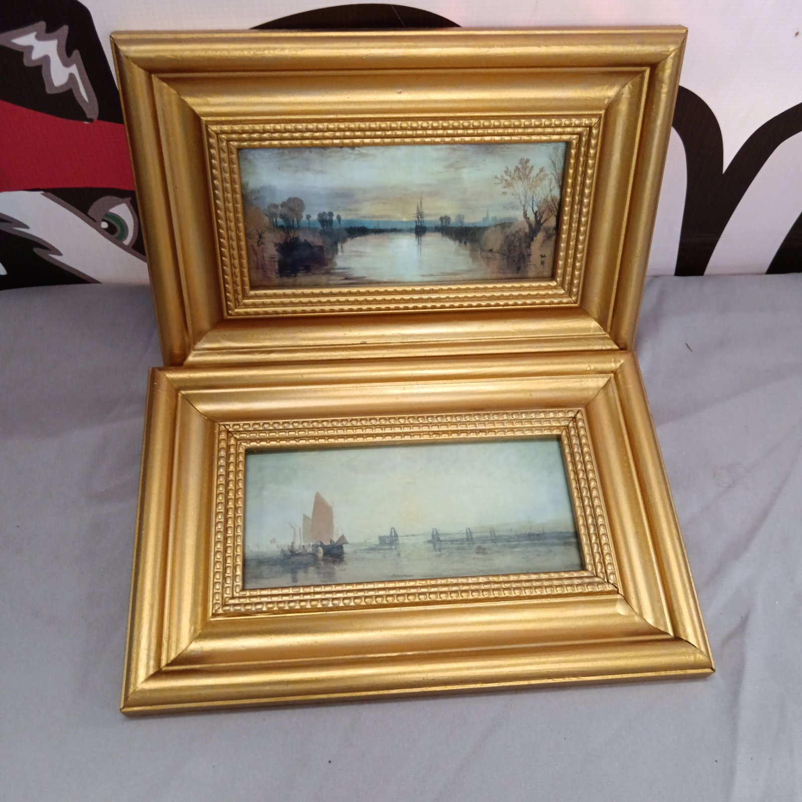 Two miniature gilt framed nautical prints depicting serene coastal scenes.