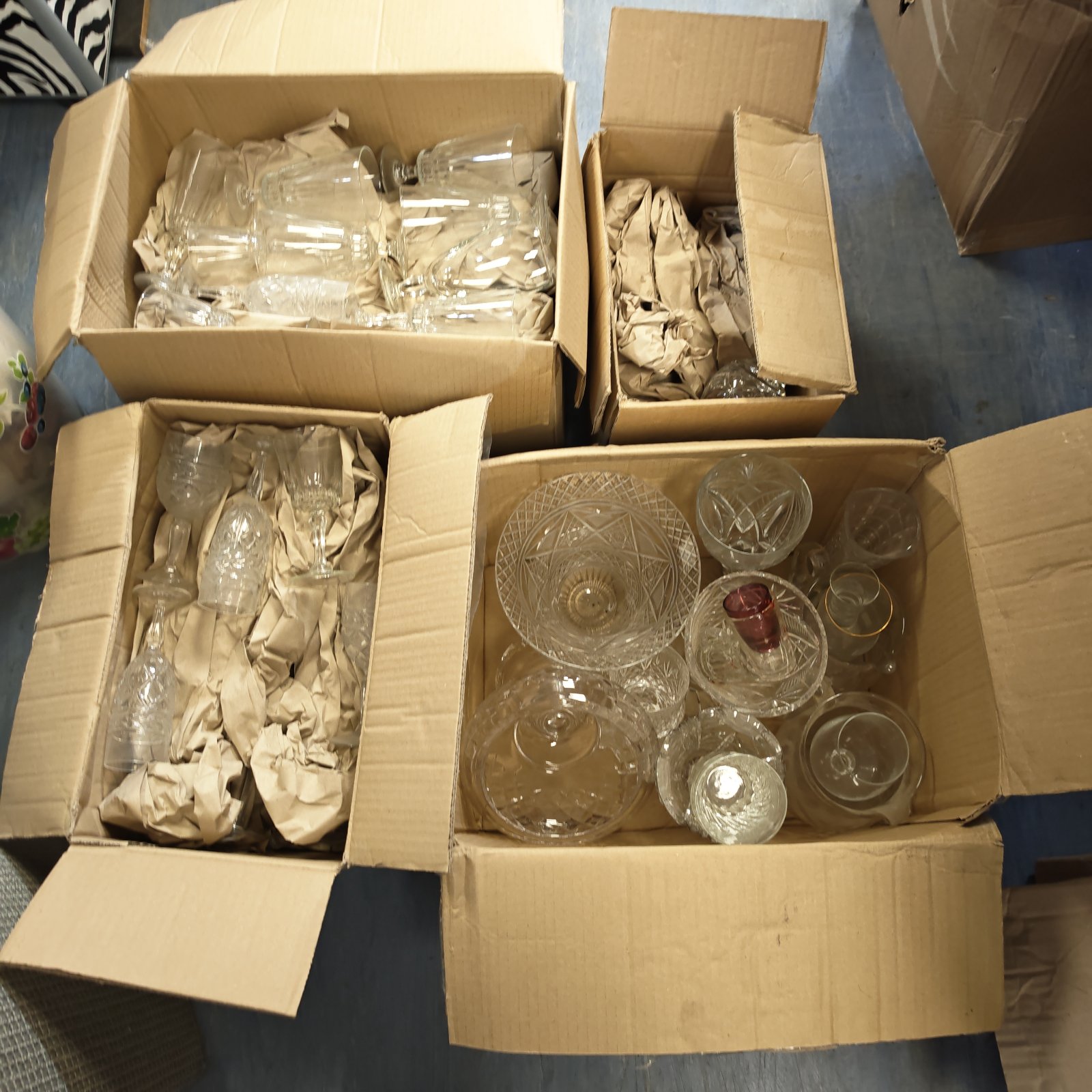 Four boxes filled with mixed vintage glassware including wine glasses and vases.