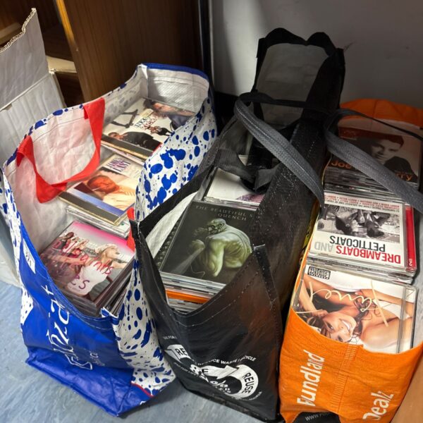 Mixed music CD lot in reusable shopping bags.