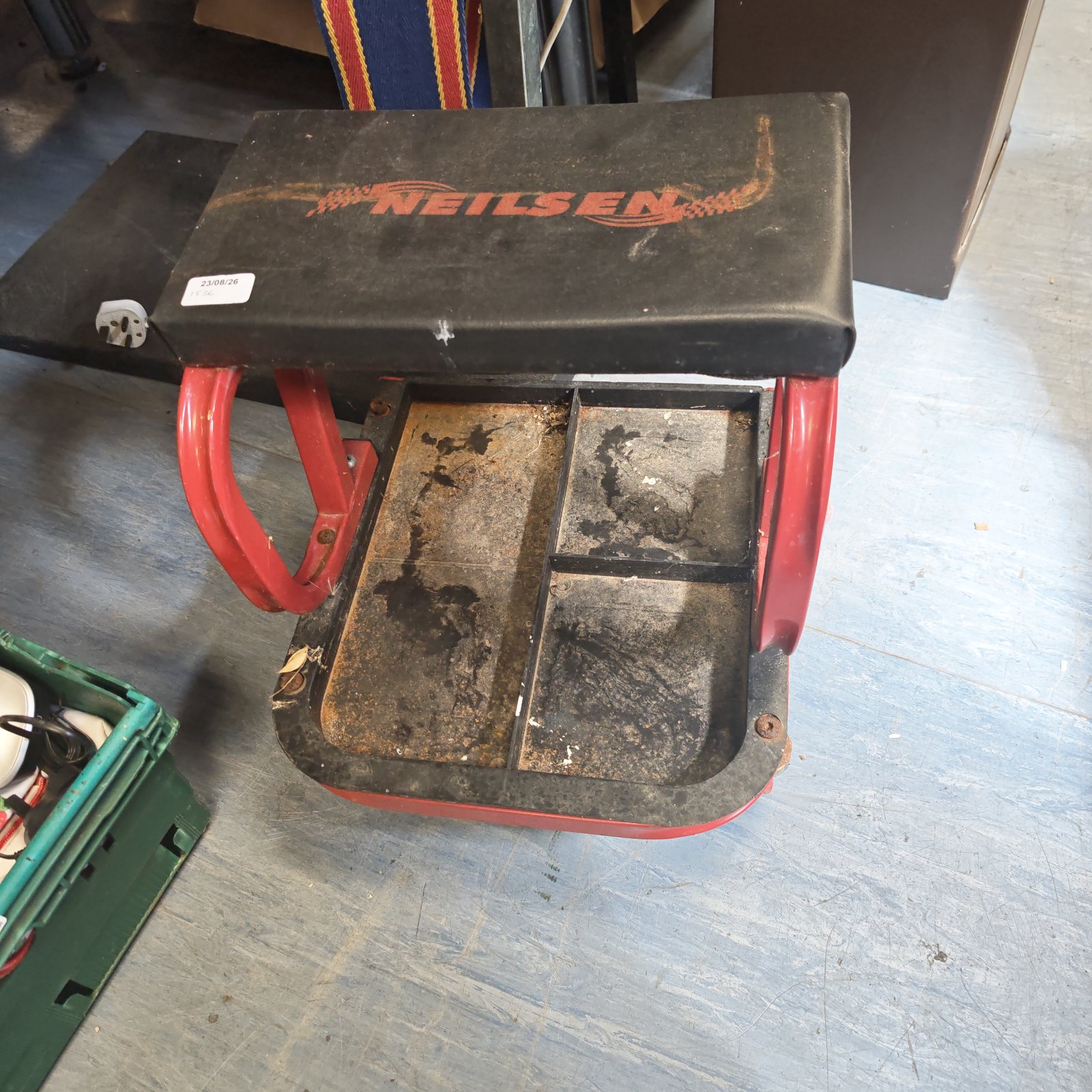 Red and black Neilsen mechanic's stool with wheels in a workshop.