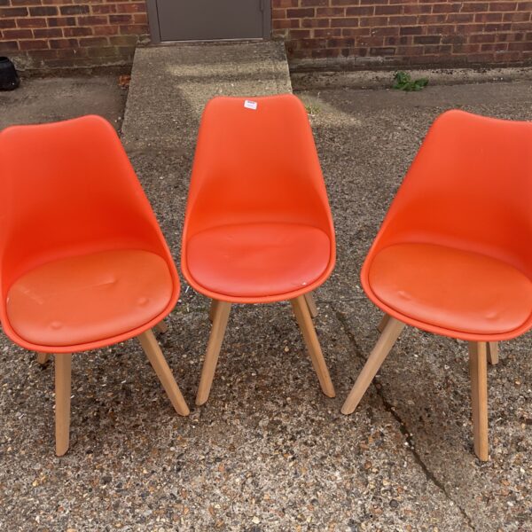 Three orange MCC Eva dining chairs with wooden legs.