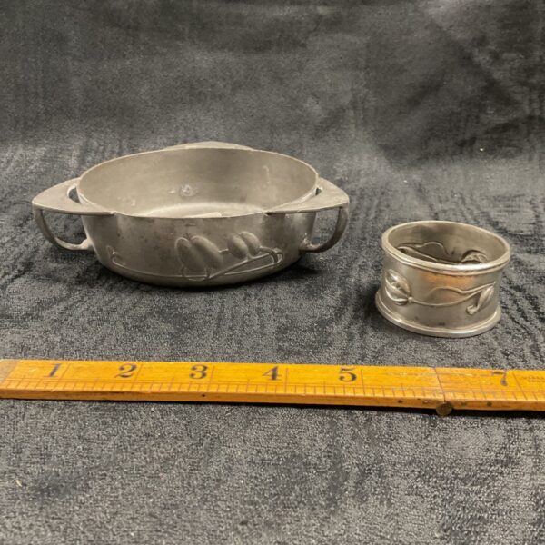 Antique pewter Archibald Knox bowl and napkin ring set on display.