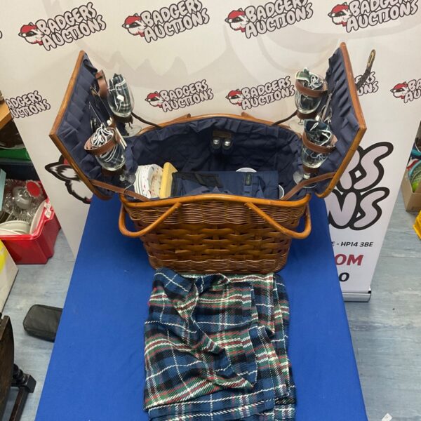 Wicker picnic basket set with blanket and dining items.