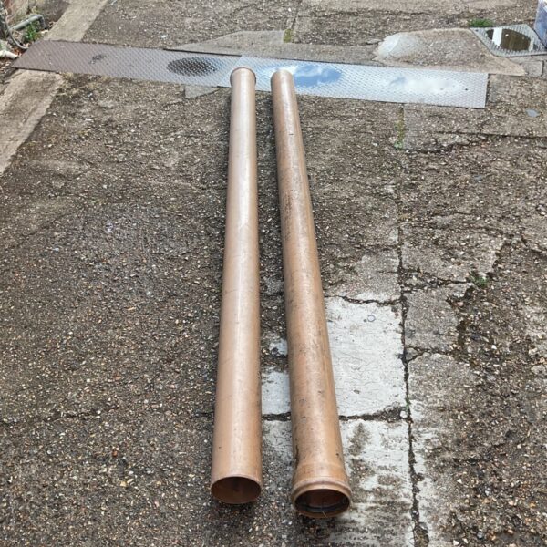 Two brown plastic drainage pipes lying on paving.