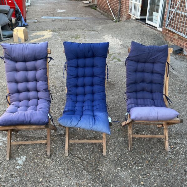 Lot of three blue cushioned recliner deck chairs in a garden.