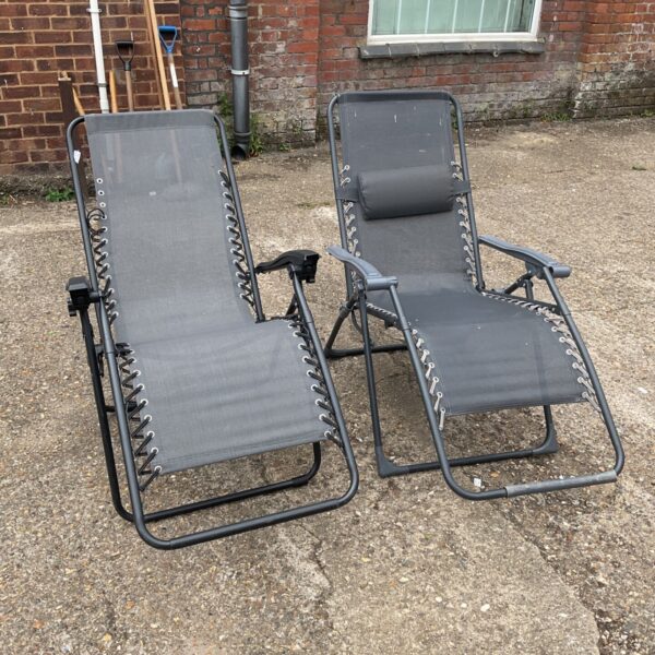 Pair of grey recliner sun chairs in a garden setting.