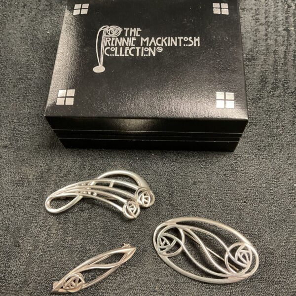 Close-up of three Rennie Mackintosh silver art nouveau brooches.
