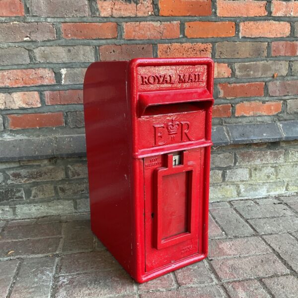 Vintage red Royal Mail post box against brick wall.
