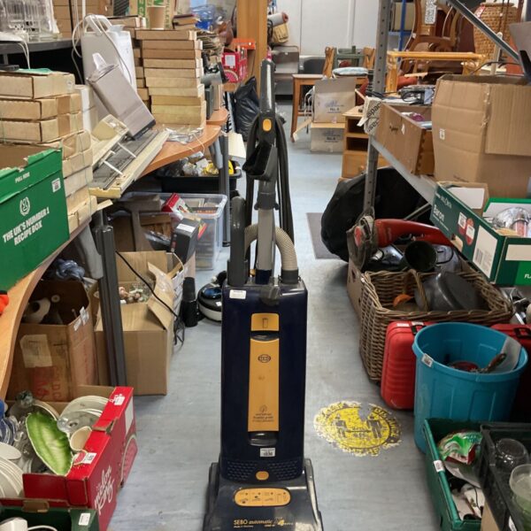 Used Sebo Automatic X4 upright vacuum cleaner in a cluttered space.