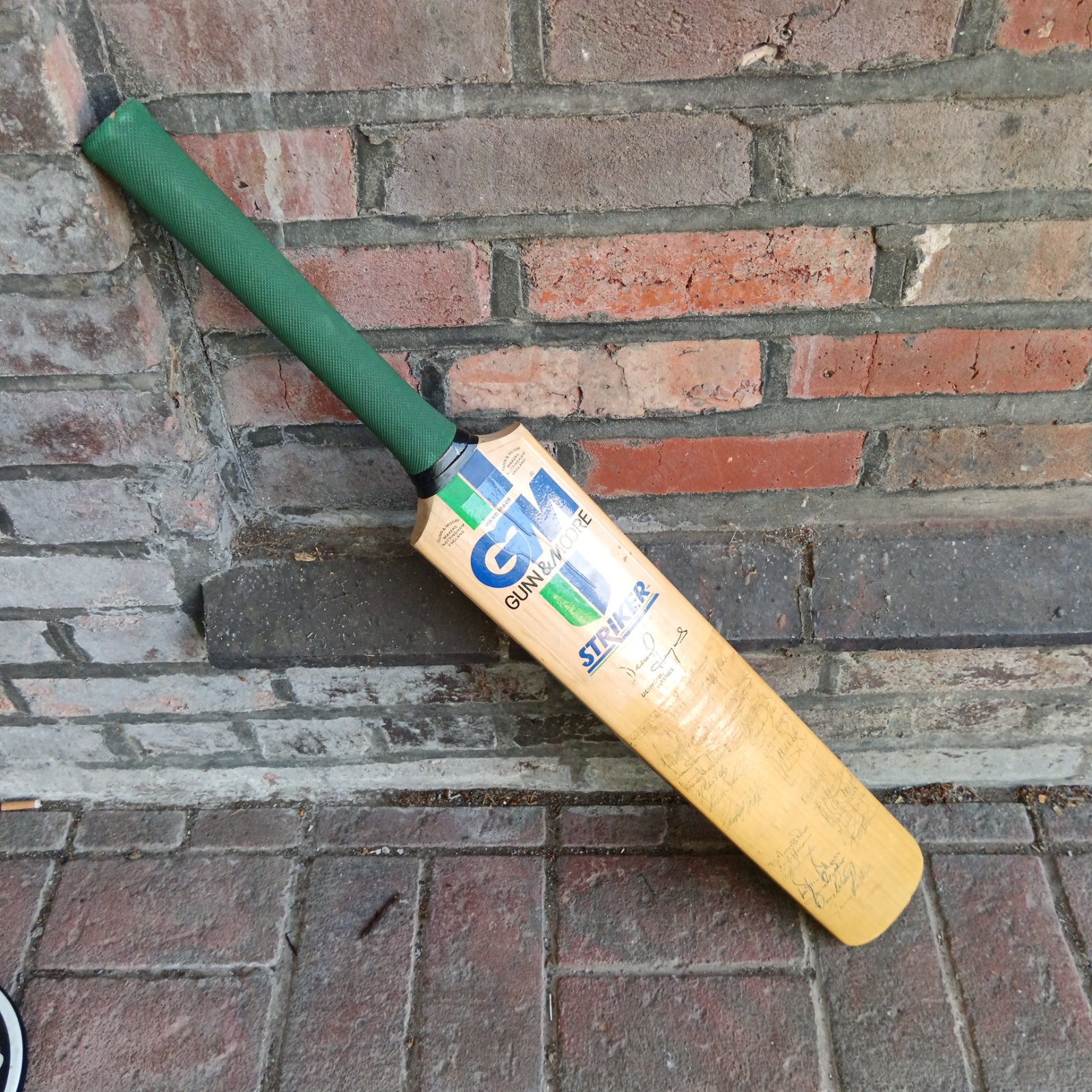 Signed cricket bat leaning against a brick wall.