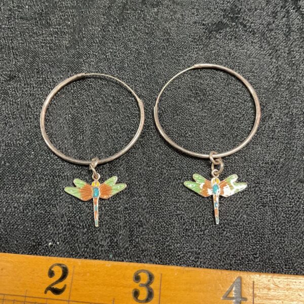 Close-up of silver hoop earrings with colourful dragonfly pendants.