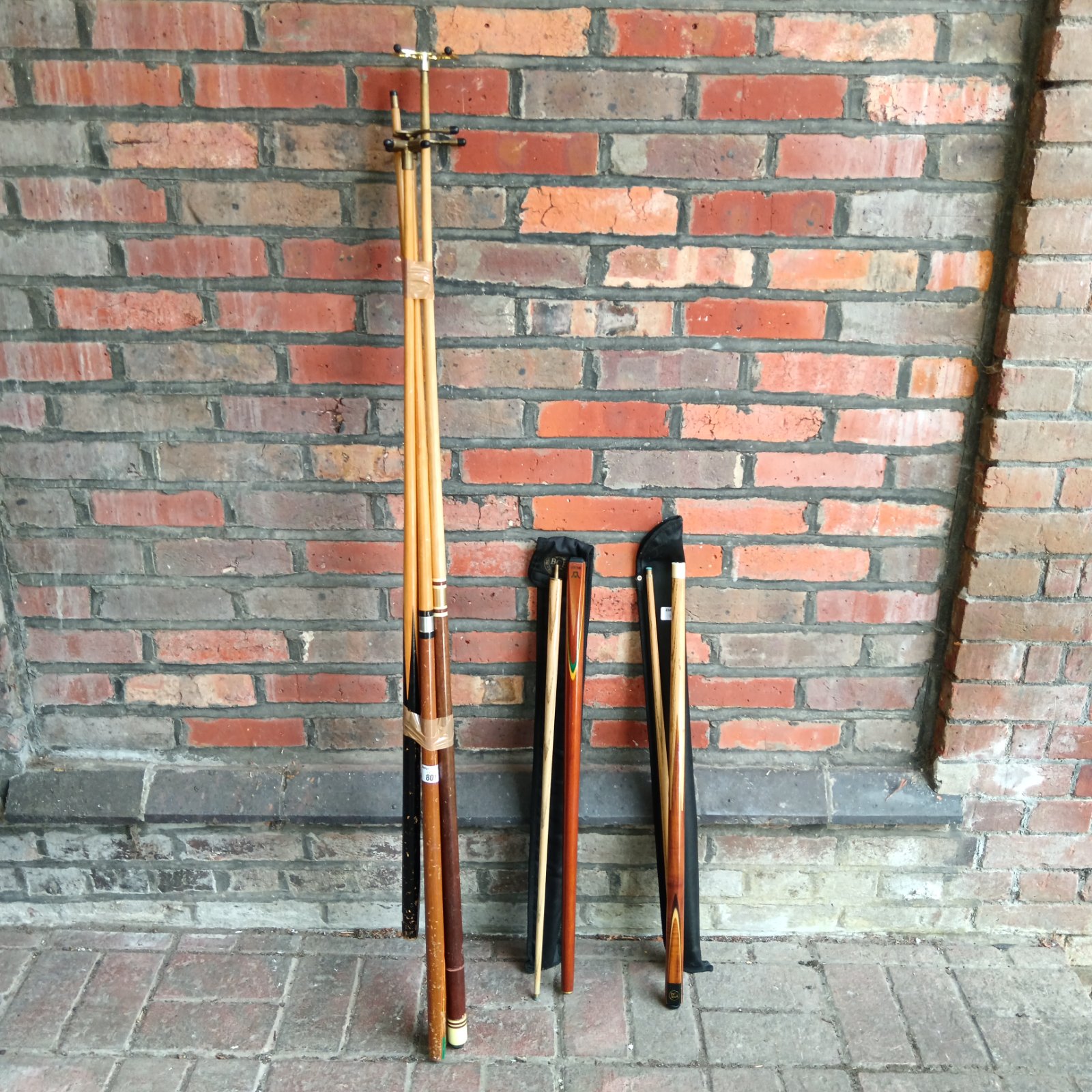 Snooker cues and bridges leaning against a brick wall.