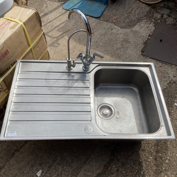 Stainless steel kitchen sink with tap, showing signs of use.