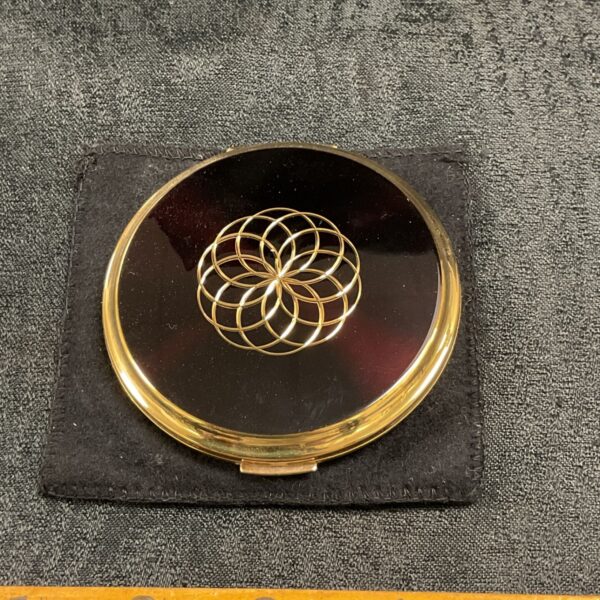 Vintage Stratton compact with a gold floral design, displayed on a dark surface.
