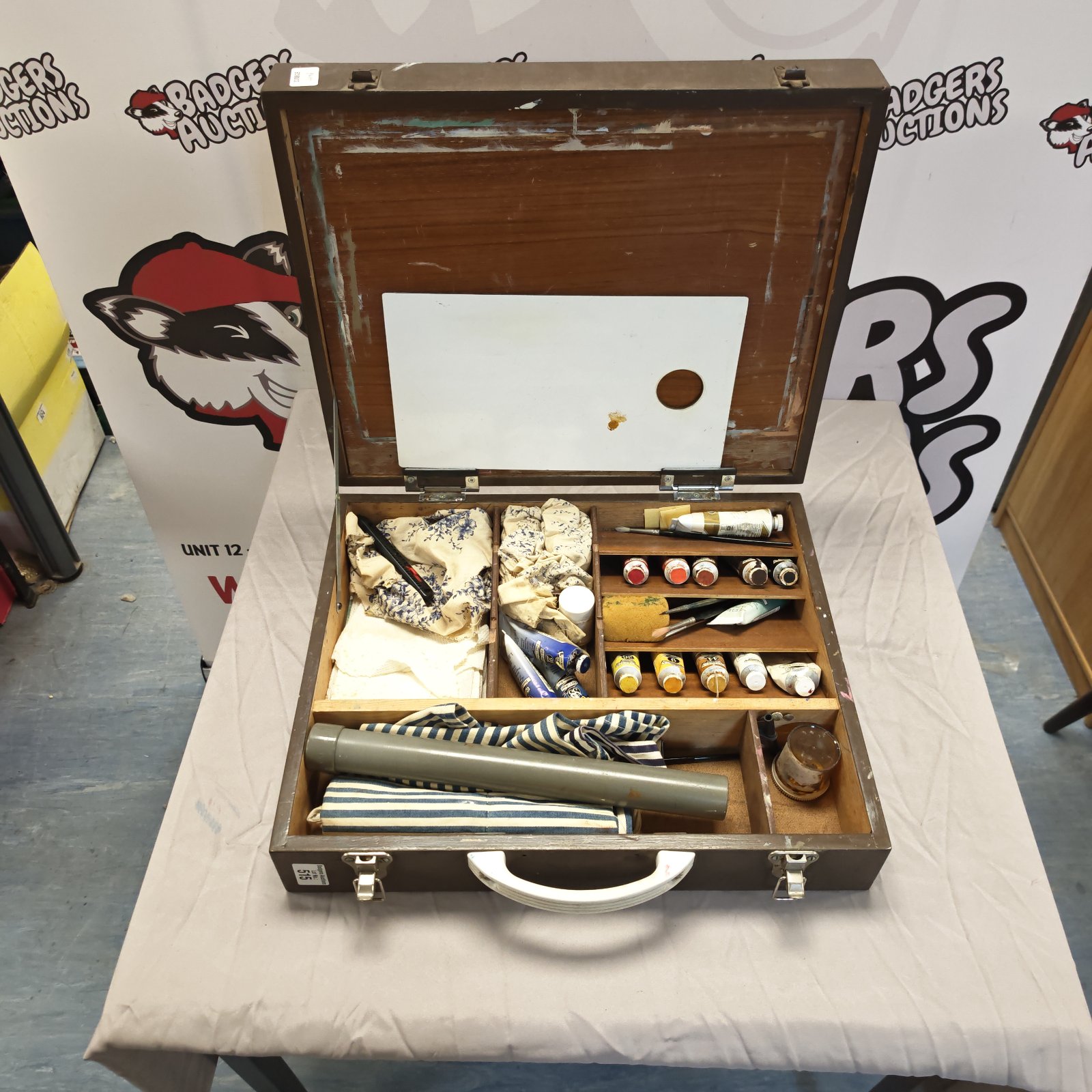 Open vintage artist easel with paints and brushes inside.