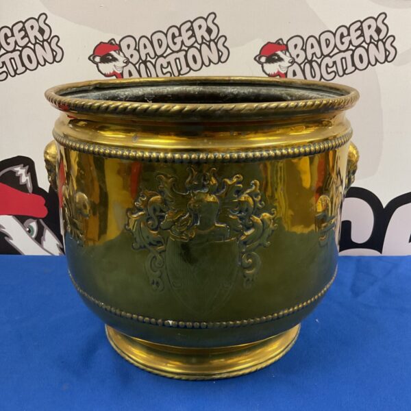 Ornate vintage brass pot with head handles and coat of arms.