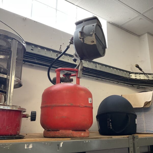 Vintage gas lamp with a hooded burner and cylindrical tank.