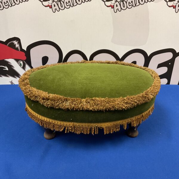 Vintage green velvet footstool with tassel fringe and wooden legs.