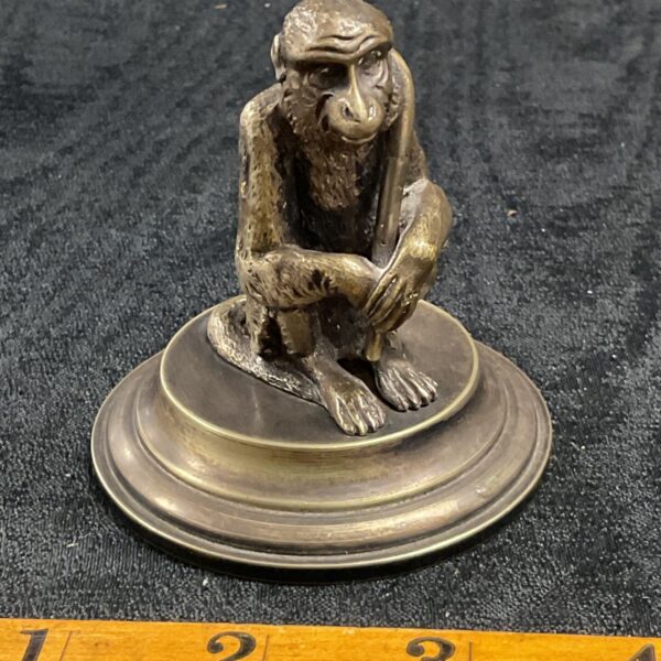 Vintage whitemetal monkey paperweight on a reflective surface.