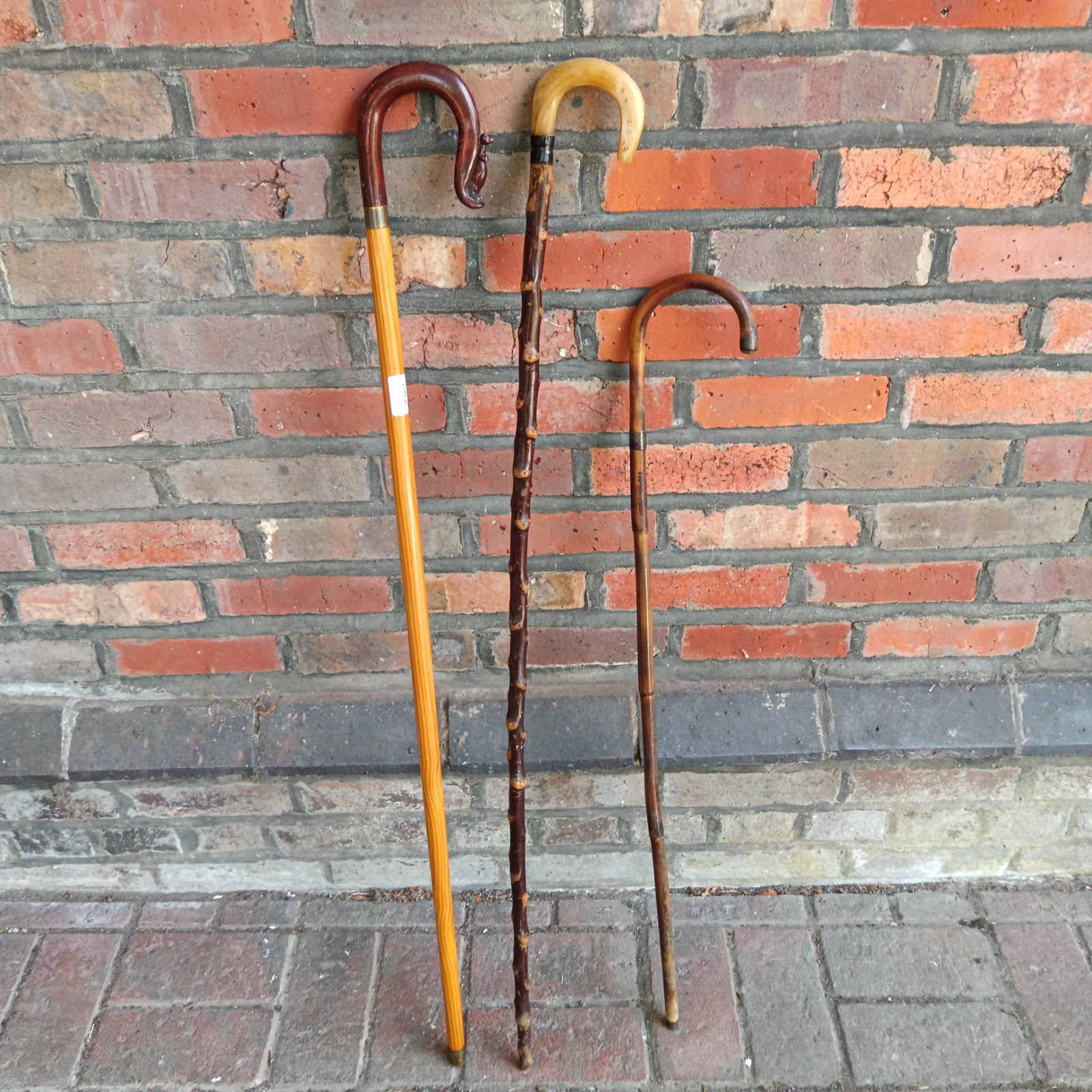 Group of three vintage walking sticks against brick wall.