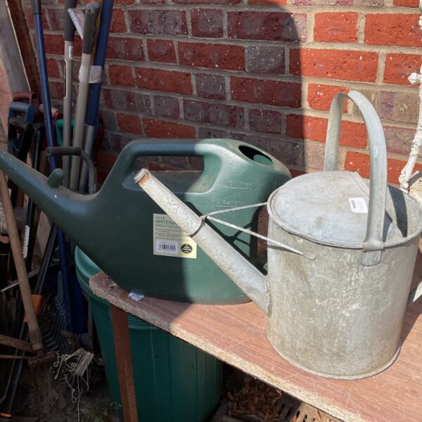 Pair of vintage galvanised watering cans in a garden setting.