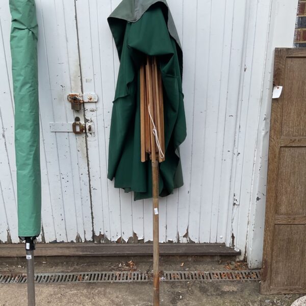 Vintage wooden parasol with a green canopy against a weathered wall.