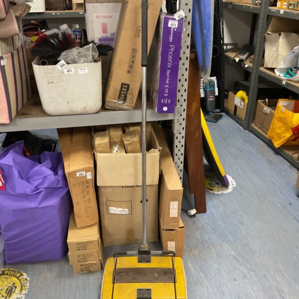Vintage yellow and chrome manual carpet sweeper in a cluttered space.