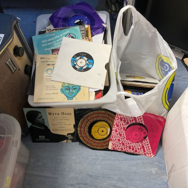 Mixed lot of vintage 7 inch vinyl records in a clear container.