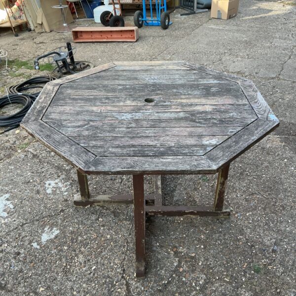 Weathered octagonal garden table with parasol hole in a garden setting.