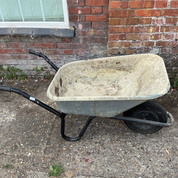 Weathered wheelbarrow with a black steel frame in a garden setting.
