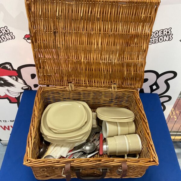 Vintage wicker picnic basket filled with plates and cutlery.