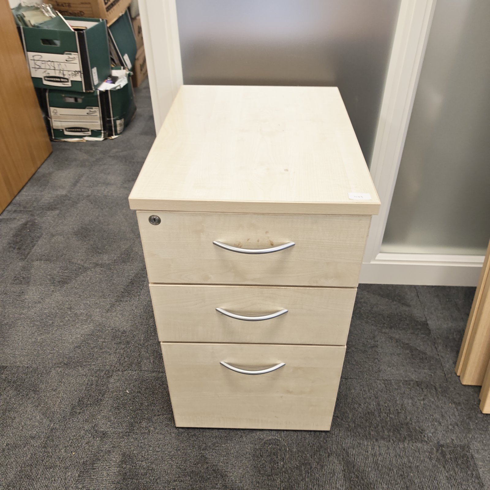 Light wood three-drawer filing cabinet for office storage.
