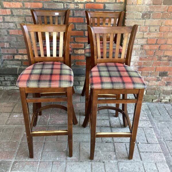 Four wooden bar stools with plaid seats in a kitchen setting.