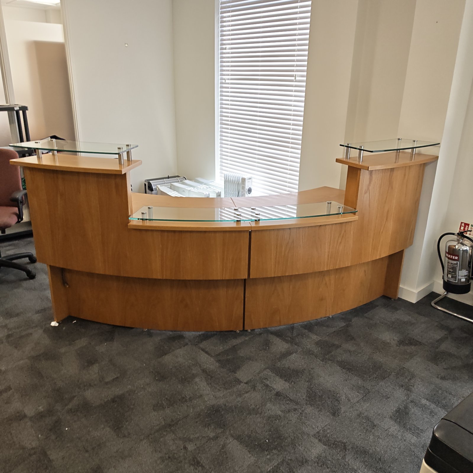 Large wooden reception desk with glass shelving in an office setting.