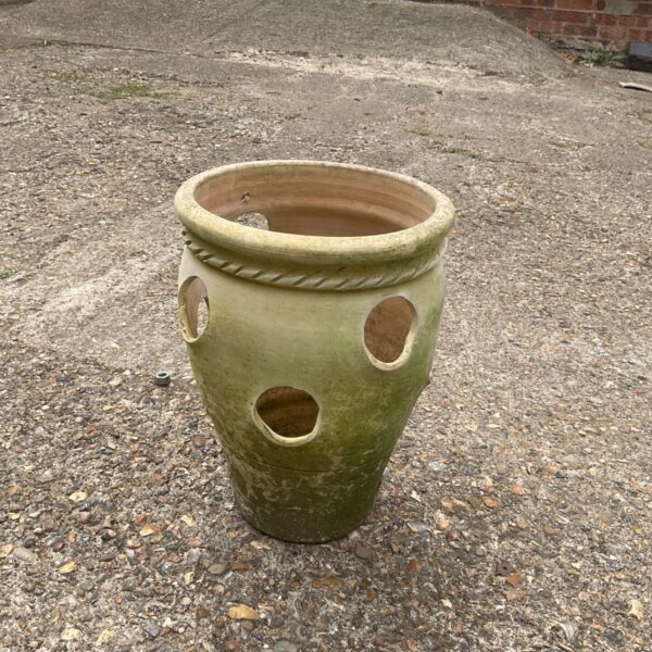 Terracotta strawberry planter with multiple planting pockets in a garden setting.