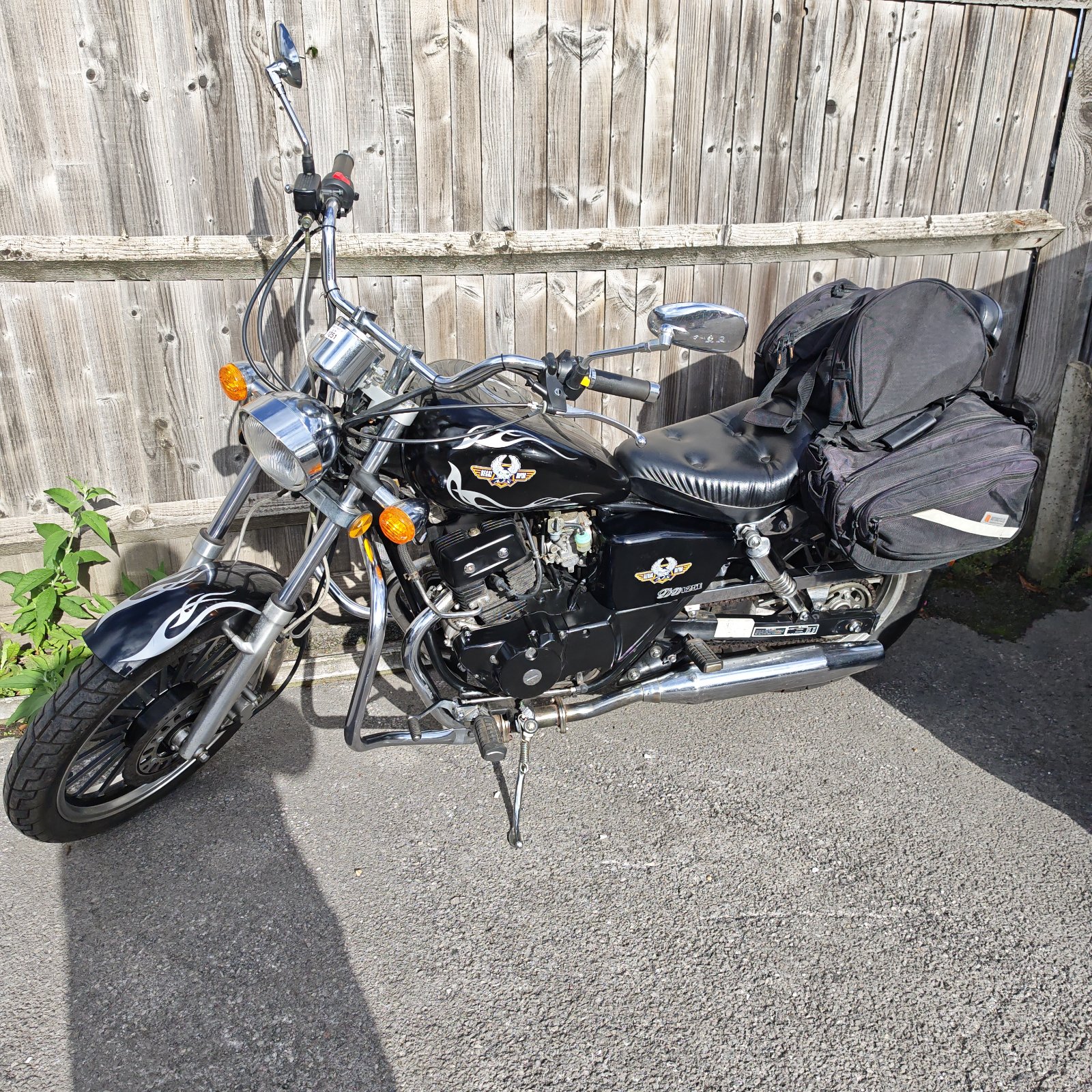 Black AJS Regal Raptor 125 motorcycle with saddlebags parked outside.