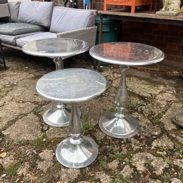 Three aluminium pedestal side tables in a garden setting.