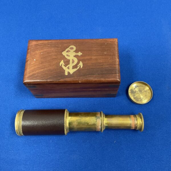 Antique nautical telescope in wooden box with anchor detail.