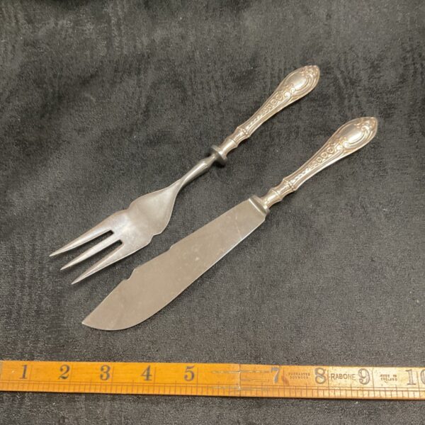 Antique silver handled fish knife and fork set on a ruler.