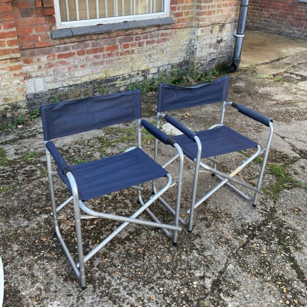Two blue folding camping chairs in a garden setting.
