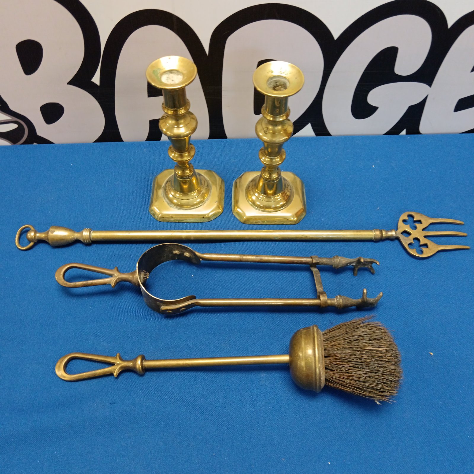 Antique brass fireplace tools and candlesticks on a patterned background.