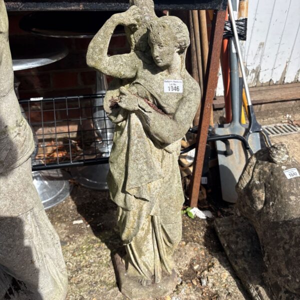 Weathered cast stone garden statue of a woman in a garden setting.