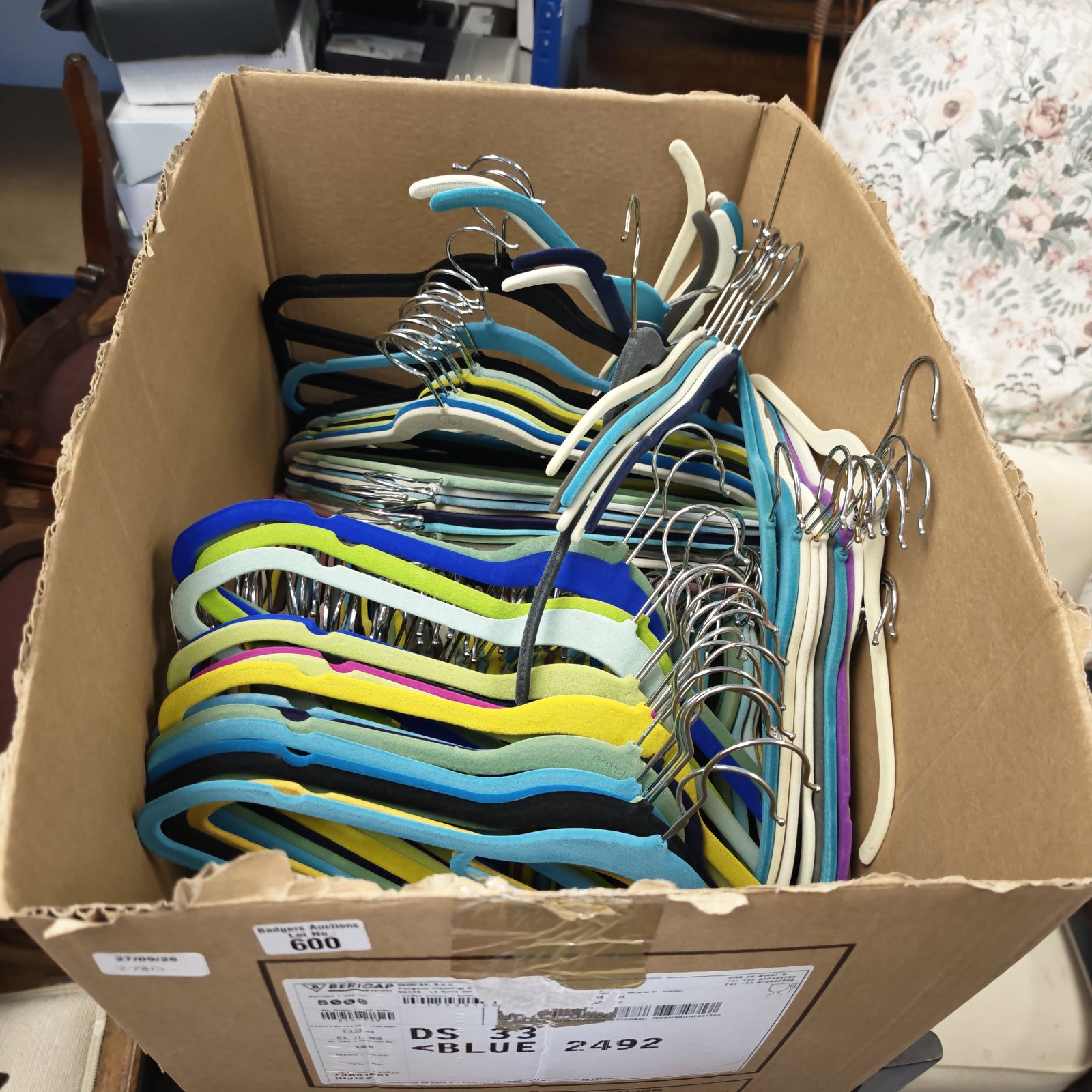 Box of colourful plastic clothing hangers for wardrobe storage.