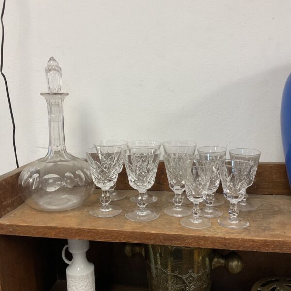 Vintage cut glass decanter and sherry glasses set on a wooden surface.