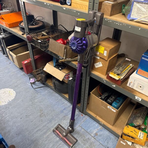 Dyson V6 Animal cordless vacuum cleaner with accessories on a shelf.