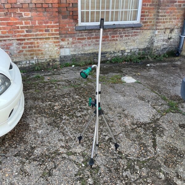 Telescopic garden sprinkler lance with tripod stand in a garden setting.