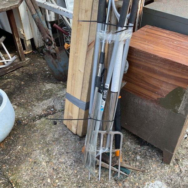 Bundle of rusty garden tools leaning against a wall.