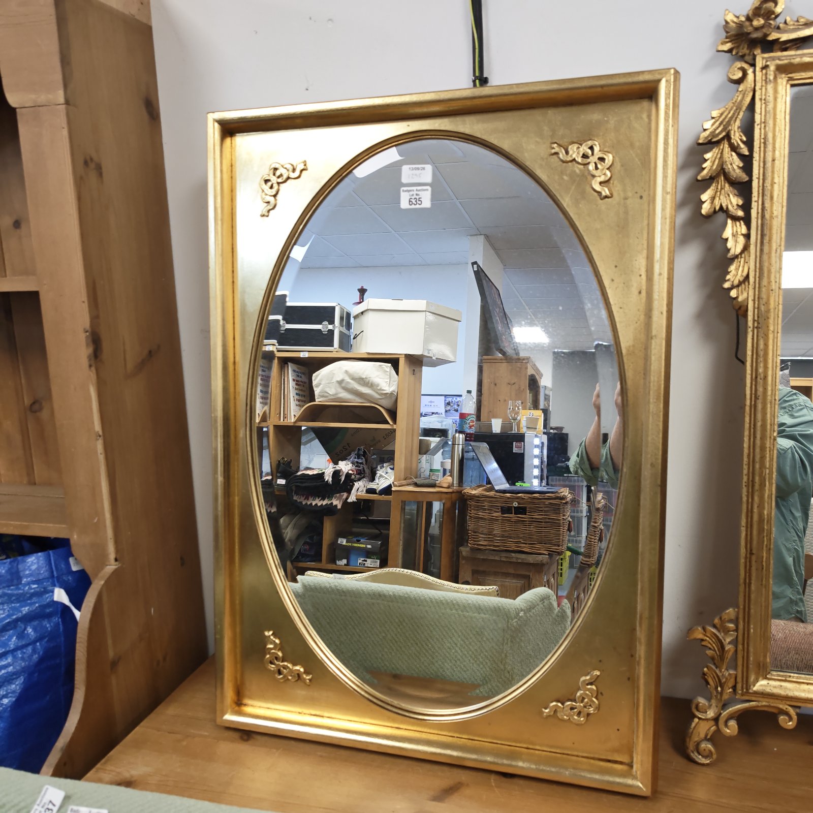 Antique gilt wall mirror with oval glass and ornate frame.